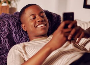 Imagem de uma mulher sorrindo enquanto segura o celular com homem sorrindo ao seu lado
